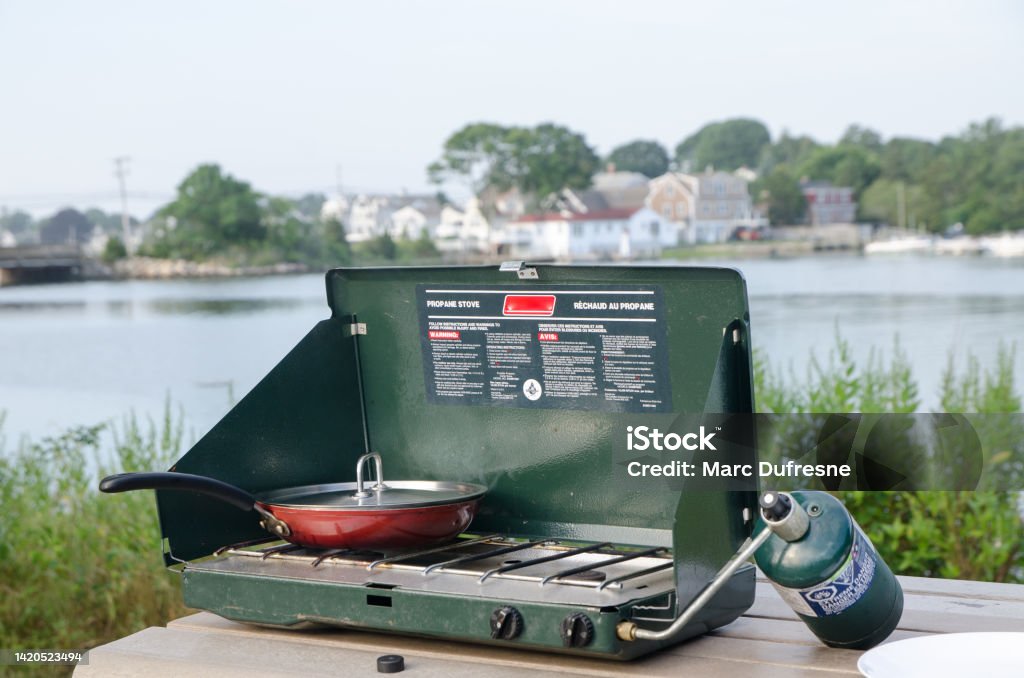 Camping propane stove with skillet Camping propane stove with skillet on a picnic table close to a lake during summer day Boiling Stock Photo