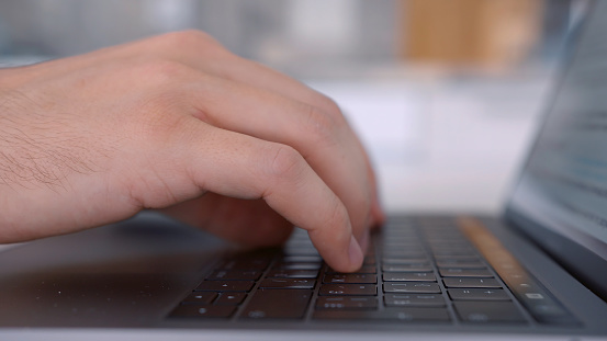 Side view of hands pressing keys of black laptop keypad. Close up of a keayboard and man hands typing on modern computer on blurred background.
