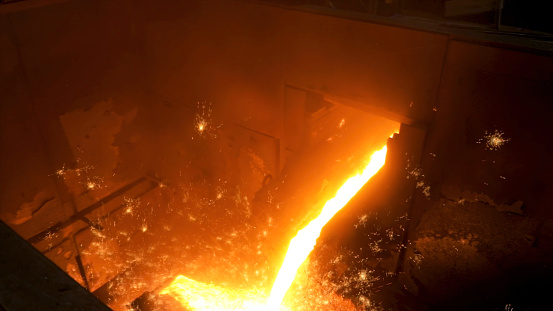 Close up for molten metal poured from ladle for casting at the foundry. Smelting of metal casting, metallurgical production at the hot shop of a factory.