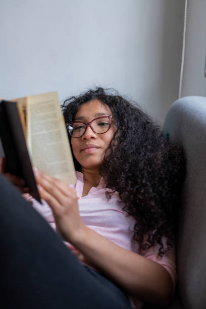 istock Beautiful curly latin woman enjoying reading at home while lying on her sofa 1420529183