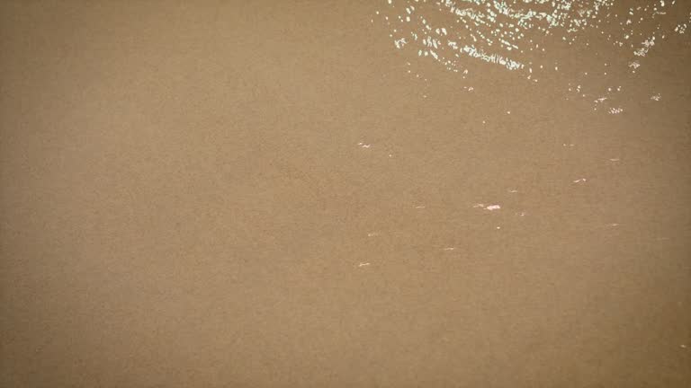 Close up view of woman hand drawing heart with finger on sand at beach and it washed away by soft waves