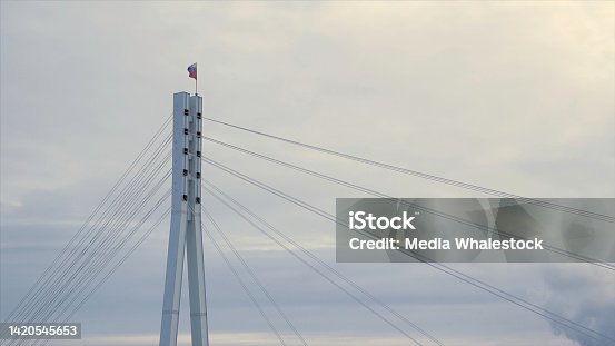 istock Russian Federation flag fluttering in the wind on the top of the bridge. Stock. Russian flag on the top of a bridge on grey, cloudy sky background. 1420545653