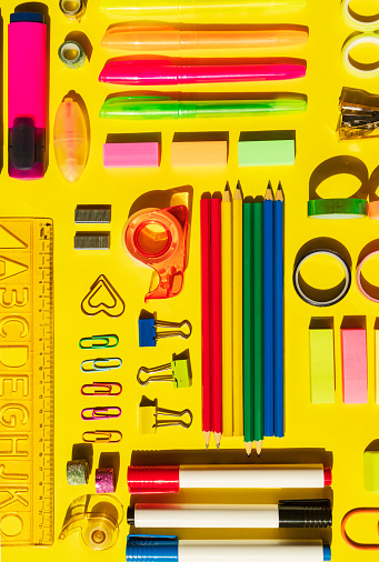 Office and school supplies arranged on yellow background