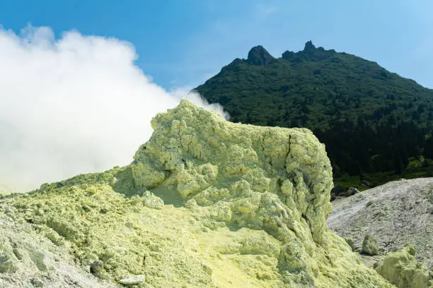 bright smoking fumarole with sulfur deposits against the background of the Mendeleev volcano peak on the island of Kunashir