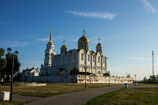the ancient white-stone Assumption Cathedral with a bell tower on a sunny summer morning in old town Vladimir and blue sky