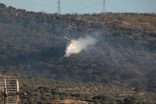 Plasencia, Spain - June 29, 2022: A small yellow hydro plane for fire extinction flying to pour water on a fire and thus put it out with deep blue sky on background
