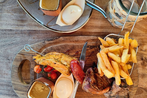 Mixed grill menu on a restaurant table with Pork tenderloin, beef tenderloin, chicken and chorizo ​​sausage served with chimmichurri and fries. There are no people or trademarks in the shot.