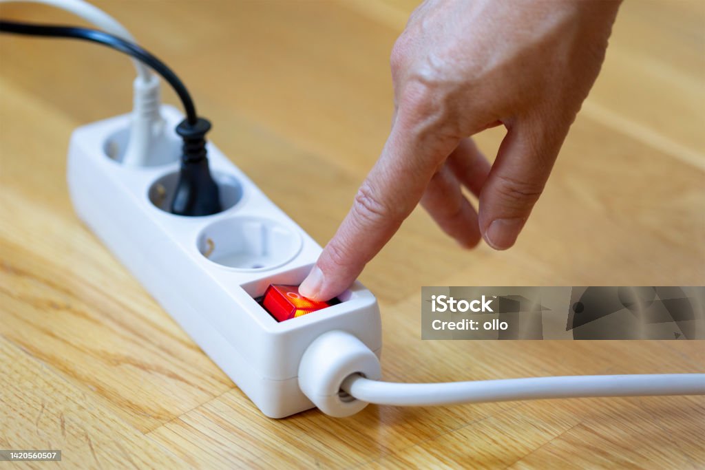 Pressing the red button of a white power strip on wooden background Pressing red button of a white power strip on wooden background - energy saving Gang Socket Stock Photo