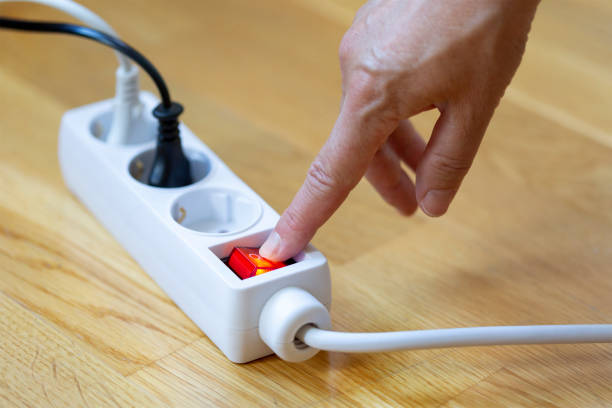 Pressing the red button of a white power strip on wooden background stock photo