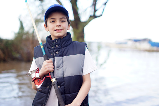 Cheerful teenage boy holding catch freshwater fish in hands on weekend