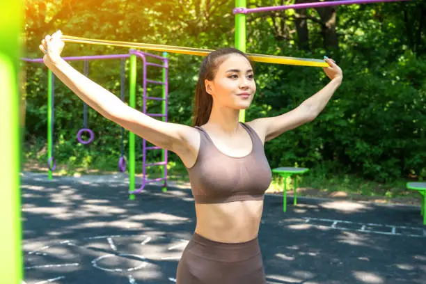 Young asian woman training with resistance band at the street sports ground.