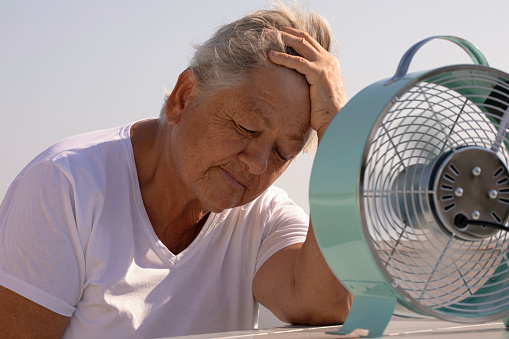 Elderly woman cools down with fan during the summer heat.