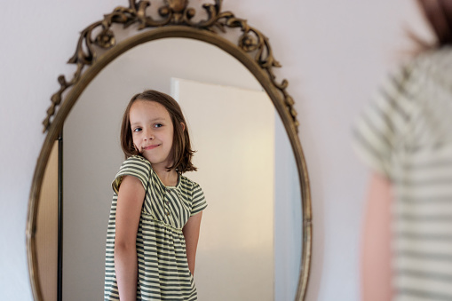 Happy little girl is standing in front of a mirror at home