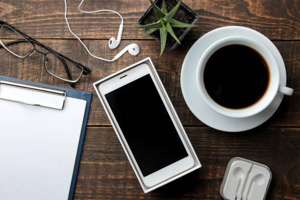 istock Smartphone white and a cup with coffee glasses and a blank on a brown wooden table. view from above 1420572305