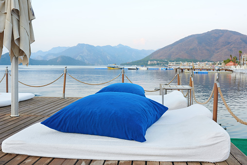Large blue pillows and soft mattresses on a wooden platform. Comfortable sun loungers for a beach holiday. Tranquility on the sea in the bay of Marmaris. Turkey, summer, beach vacation.