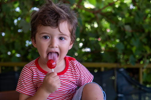 Boy wearing red striped t-shirt licking red lollipop