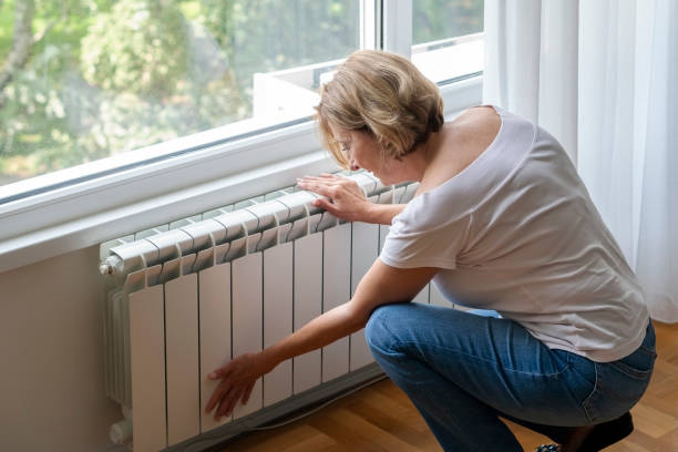Senior woman touching cold home radiator stock photo