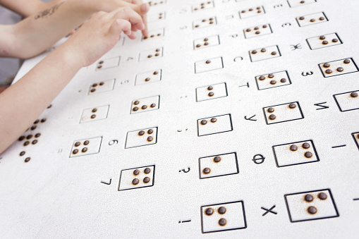 Children's hands read Braille in the open air. Tactile reading of the letters of the Ukrainian alphabet (Cyrillic) in Braille in a public park