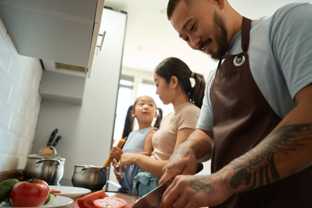 istock Man cuts tomatoes while woman and a girl cook spaghetti 1420585930