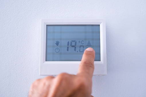 one hand adjusting the touch panel of a heating thermostat setting the temperature to 19 degrees celsius, energy saving, sustainability, selective focus