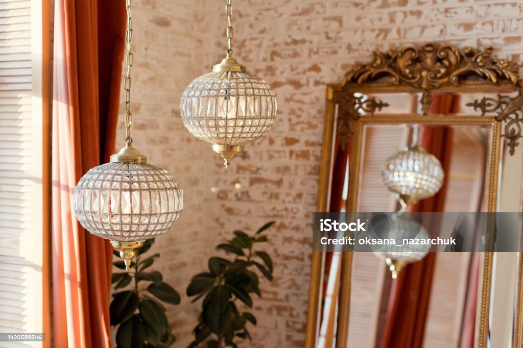 Interior with vintage mirror and chandelier Interior in oriental style with vintage golden mirror and crystal chandelier on a brick wall background Mirror - Object Stock Photo