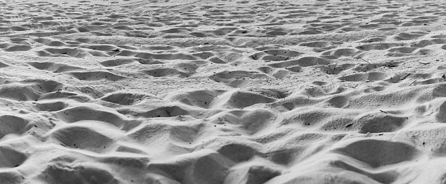 Panoramic shot of sand on a beach near a lake in black and white.