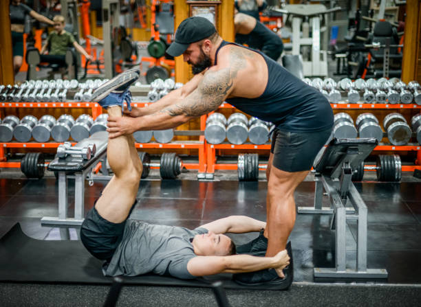 istock Man doing exercises in the gym with a man trainer athletic physique 1420606114