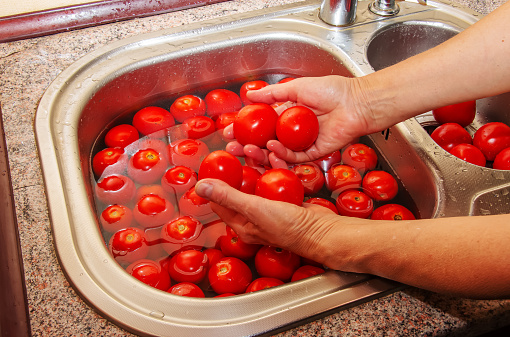 A woman's hands wash tomatoes under running water in the kitchen sink.