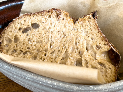 Horizontal closeup photo of a slice of sourdough bread made with wheat flour and fermented Koji rice porridge, on a brown paper napkin in a ceramic bowl.