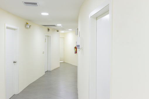 Hallway of a building with several doors and access to different rooms, all in white and ceramic floor. Vertical photography.