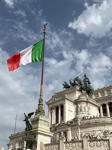Dramatic portrait of the Italian flag flying in the wind on a beautiful summer day. National Monument downtown Rome, Italy.