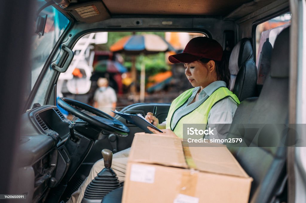 I've got just a few more stops to make Shot of a female courier writing on a clipboard while sitting in a delivery van Malaysia Stock Photo