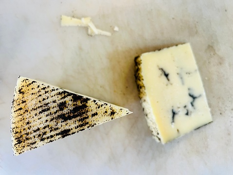 Horizontal high angle closeup photo of two wedges of Spanish cheese infused with black truffle from the region of La Mancha, Spain, on a marble slab.