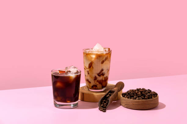 Kawa lodowa w wysokiej szklance z wylaną śmietaną i ziarnami kawy. Zestaw z różnymi rodzajami napojów kawowych na różowym stole. – zdjęcie