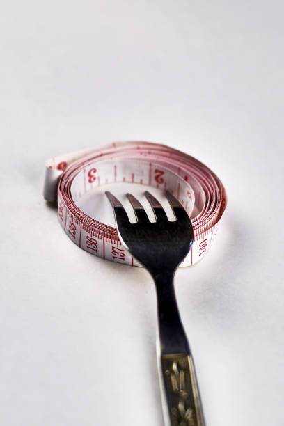 iron fork rewound with measuring tape on a white background concept diet