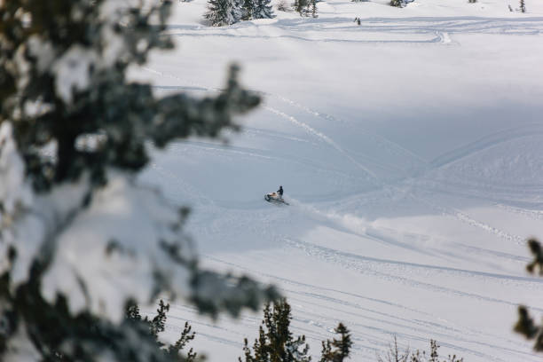 снегоход поднимается по склону горы через снежное поле - snowmobiling adventure snow travel стоковые фото и изображения