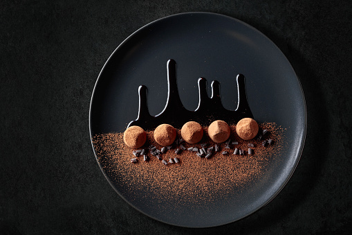 Chocolate truffles on a black plate with chocolate sauce. Top view.