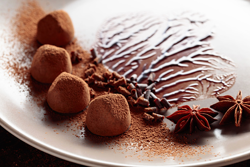Chocolate truffles on a beige plate with chocolate sauce. Sweets are sprinkled with cocoa powder, chocolate chips, and decorated with anise.