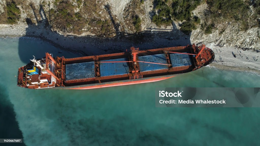 Aerial top view of an empty, red barge moored near the beautiful blue sea shore. Big Industrial ship standing near the hill with green trees. Aerial top view of an empty, red barge moored near the beautiful blue sea shore. Big Industrial ship standing near the hill with green trees Barge Stock Photo