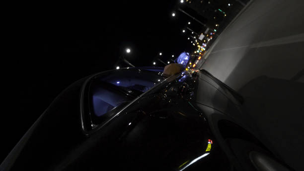 도시를 통과하는 야간 도로에서 운전하는 빠른 검은 색 자동차, 바퀴에서 볼 수, 타임랩스. 푸티지. 저녁에 바쁜 도시를 따라 움직이는 현대 차량, 도로 여행 개념. - central perspective 뉴스 사진 이미지
