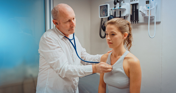 Doctor or cardiologist with stethoscope on patient chest to help, test or examine for pain in hospital or clinic room. Cardiology medical healthcare worker listening to heartbeat of sick young woman
