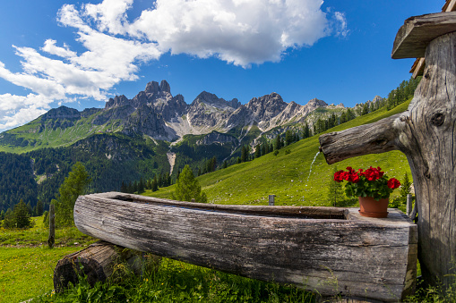 Wooden well at Idyllic summer landscape in Dachstein Mountains with view to large Bischofsmütze