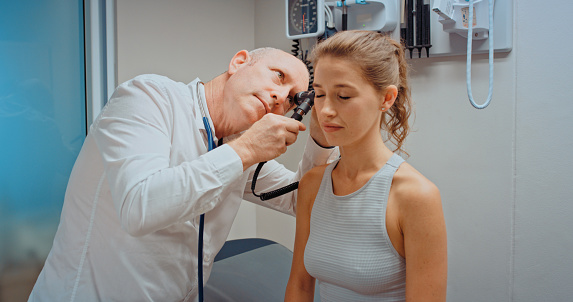 Healthcare, medicine or wellness with a doctor using an otoscope to check the ear of a patient and consulting in an appointment or checkup in a hospital. Help, trust and medical insurance in a clinic