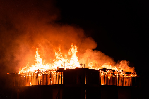 Close up of fire destroying constructing residential building rooftop at night