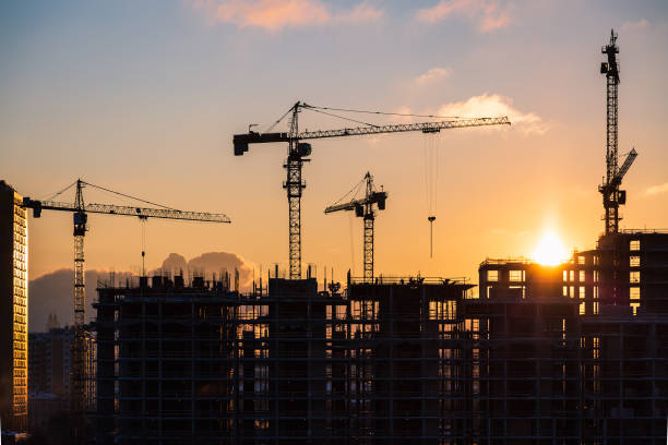 Building site at sunset Lots of tower cranes build high-rise residential building in evening time. Steel frame structure in sunlight. Industrial background with sun flare. Yellow sunset sky. property styling stock pictures, royalty-free photos & images