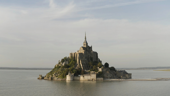 Aerial panoramic view of unique temple on the island surrounded by the sea on blue cloudy sky background. Amazing Mont-Saint-Michel castle, France.