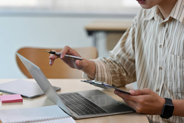 istock Cropped view businessman holding a note and a pen sitting in an office and working on a laptop, for business and technology concept. 1420683606
