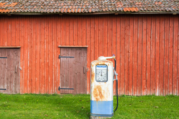 Old rusty petrol pump by a red barn in the countryside
