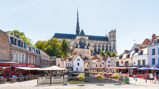 Amiens, France - August 13, 2022: Panoramic view of Notre-Dame d'Amiens cathedral overlooking the Don square lined with historic townhouses, sidewalk cafes and restaurants on a sunny summer day.