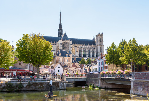 Amiens, France - August 13, 2022: Notre-Dame d'Amiens cathedral overlooks the Somme river, with the man on buoy by german sculptor Stephan Balkenhol in the foreground, on a sunny summer day.